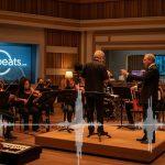 Musicians and conductor in a Brazilian TV studio, music-themed editorial photo with warm lighting